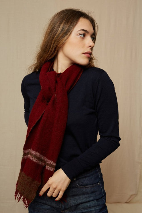 Blonde haird woman against a beige background looking away from camera with dark red Mois Mont scarf around neck 