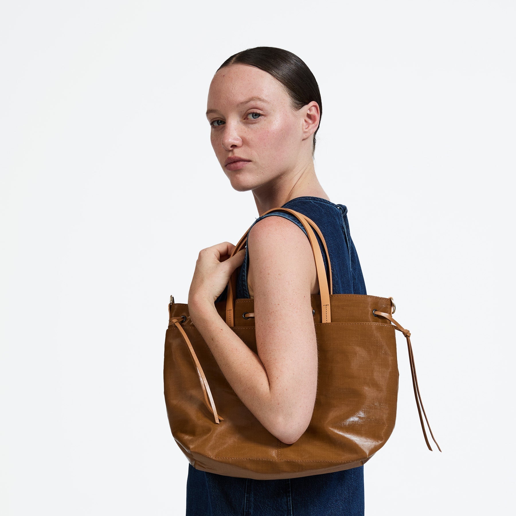 Woman holding a brown leather bag against a white background