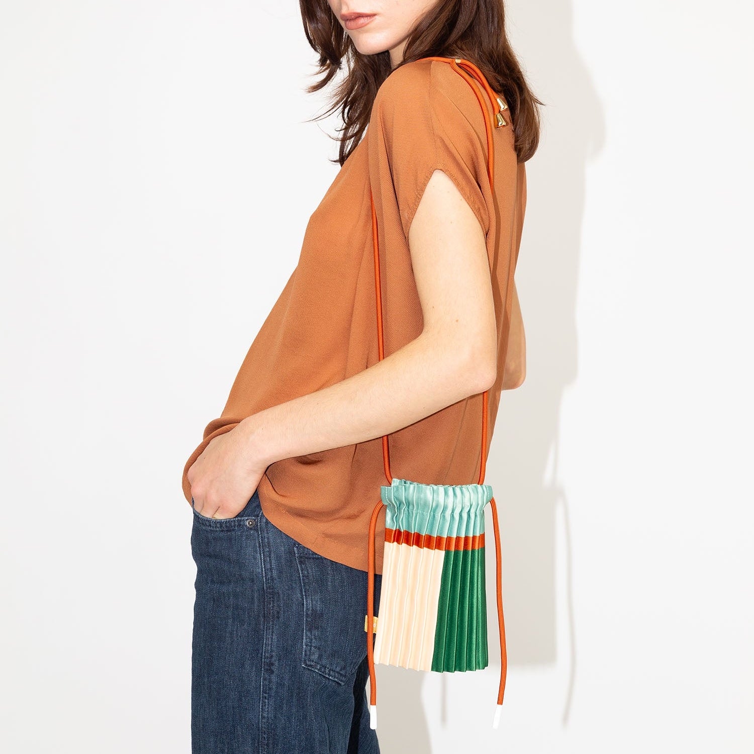 Woman wearing an orange sleeveless top with a colorful bag over her shoulder on a white background