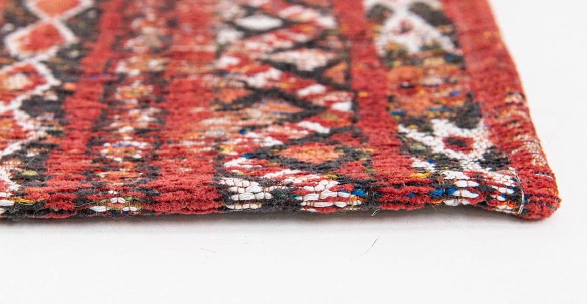 Closeup of edge of rug with Morrocan nomad pattern in red tones.