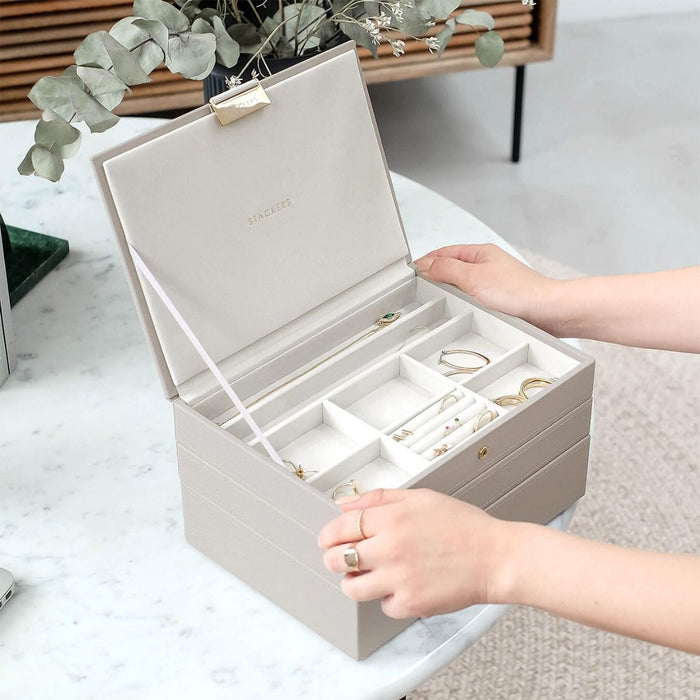 Grey stackacble jewelery boxes open in front of model on marble table. white interior with compartments 