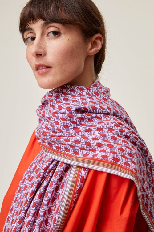 Blonde haird woman against a beige background looking away from camera with dark red Mois Mont scarf around neck 
