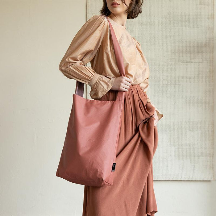 Model in silky fabrics against beige background, beige top and teracotta colour skirt with coral coloured vegan leather handbag