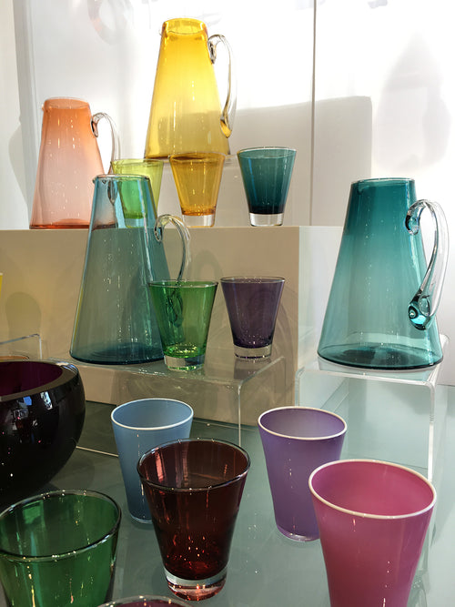 Colourful designer glasses and water pitcher on tiled table