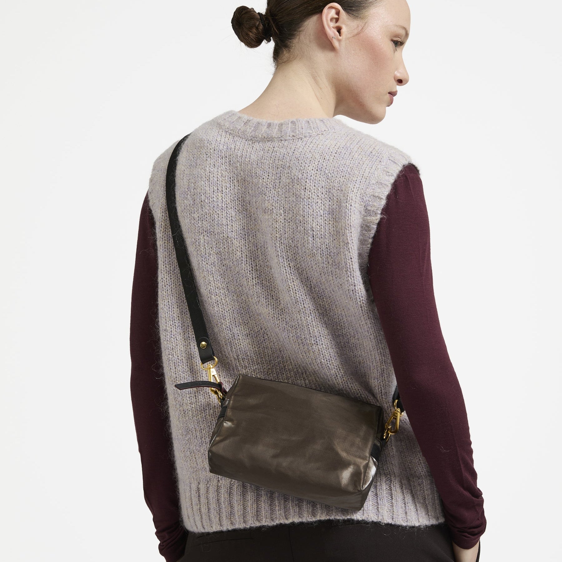 Woman wearing a gray sweater vest and maroon long-sleeve shirt with a dark handbag on a white background