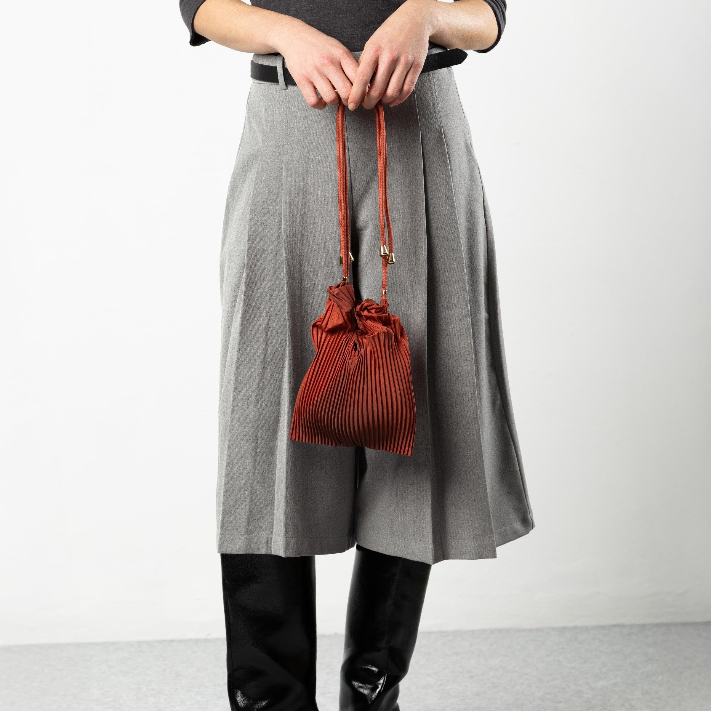 Person holding a red handbag wearing a gray skirt and black boots on a white background
