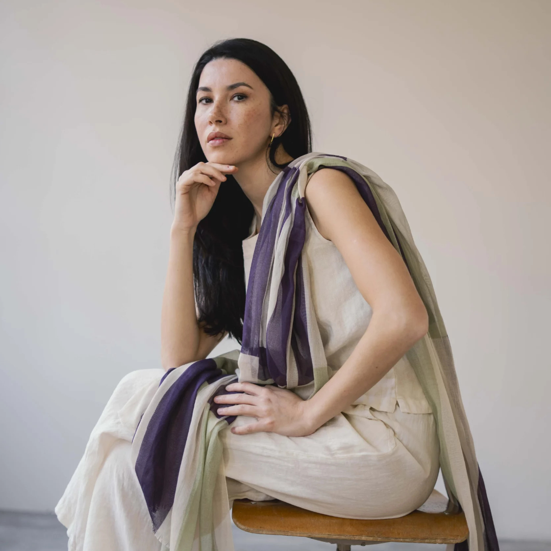 Woman sitting on a chair with a scarf draped over her shoulders against a plain background