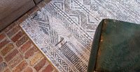 Closeup on floor view of rug with Morrocan nomad pattern in white tones with grey detail.