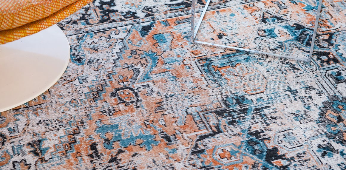 Closeup blues and oranges of rug with central medallion, rosette shaped with a stair patterned parameter.