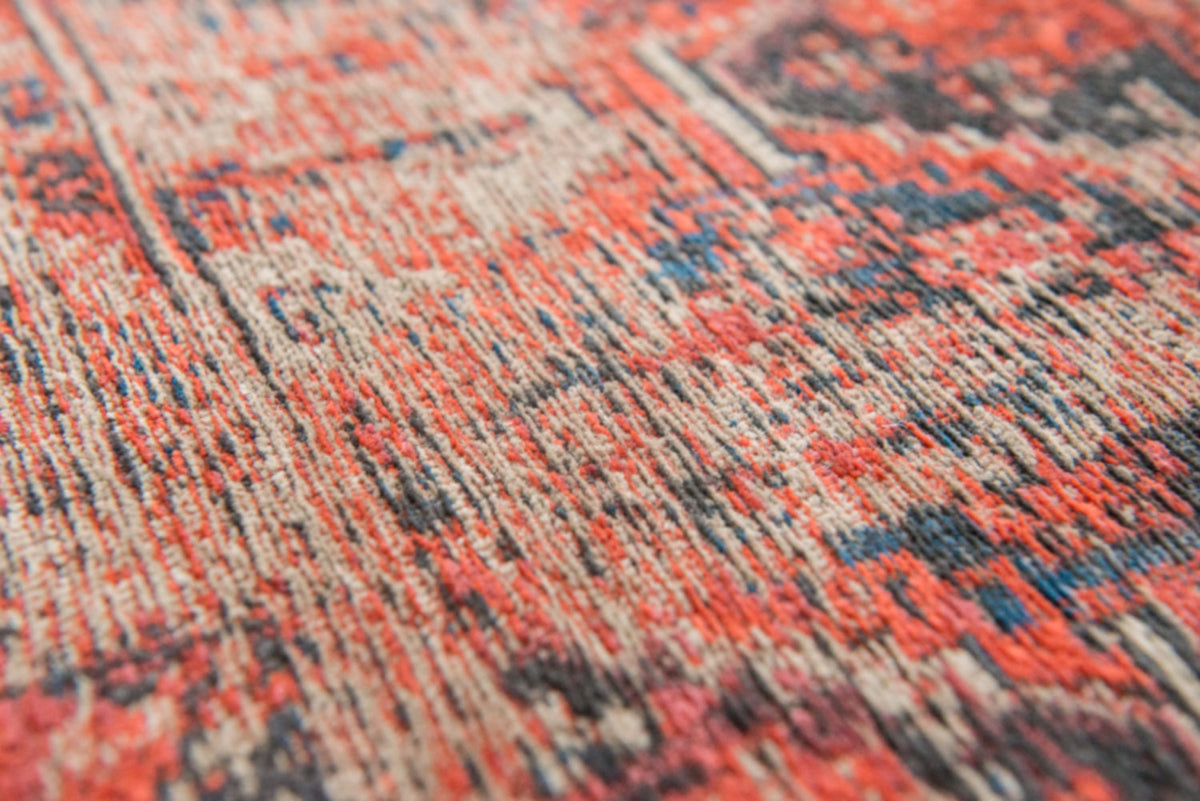 Closeup of woven detail on rich red tone distressed rug with antique pattern 