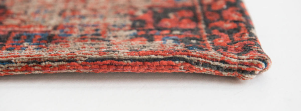 Closeup of woven edge of rich red tone distressed rug with antique pattern detail