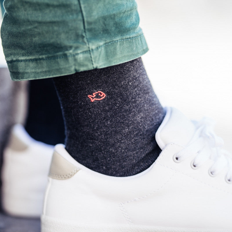 Dark grey comfortable cotton socks for men with small orange fish detail on side, on model in white sneakers. 