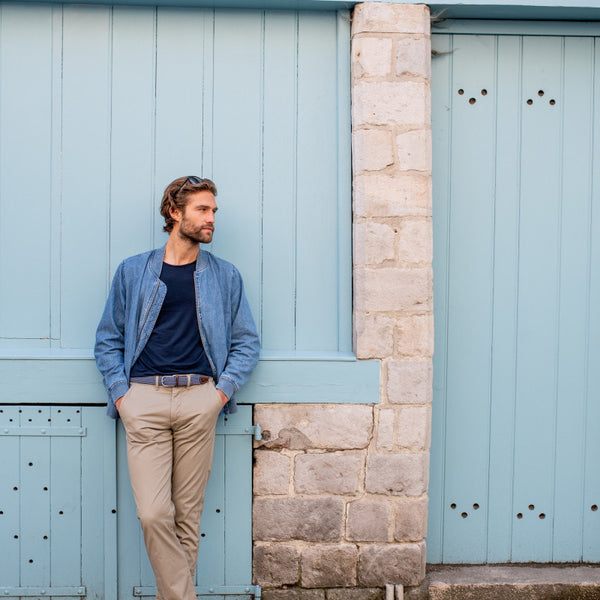 Blue and white Braided Belt with brown leather finish on model in beige pants leaning up against a blue shed