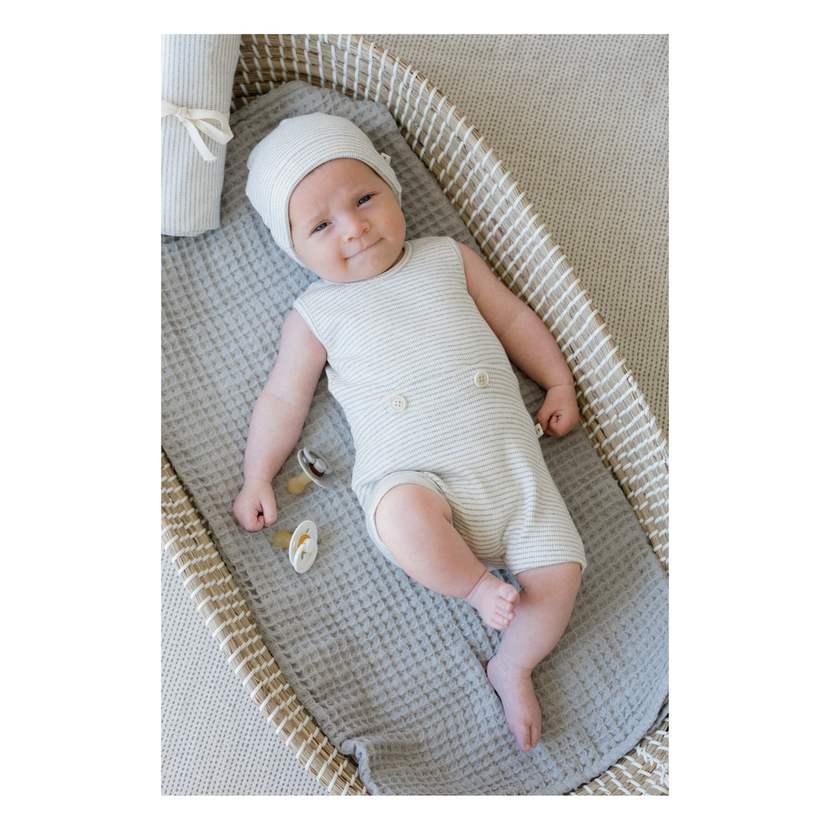 Baby lying down with white and grey beanie on