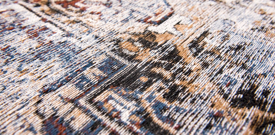 closeup of fabric on faded rug in pale tones and white with brown detail