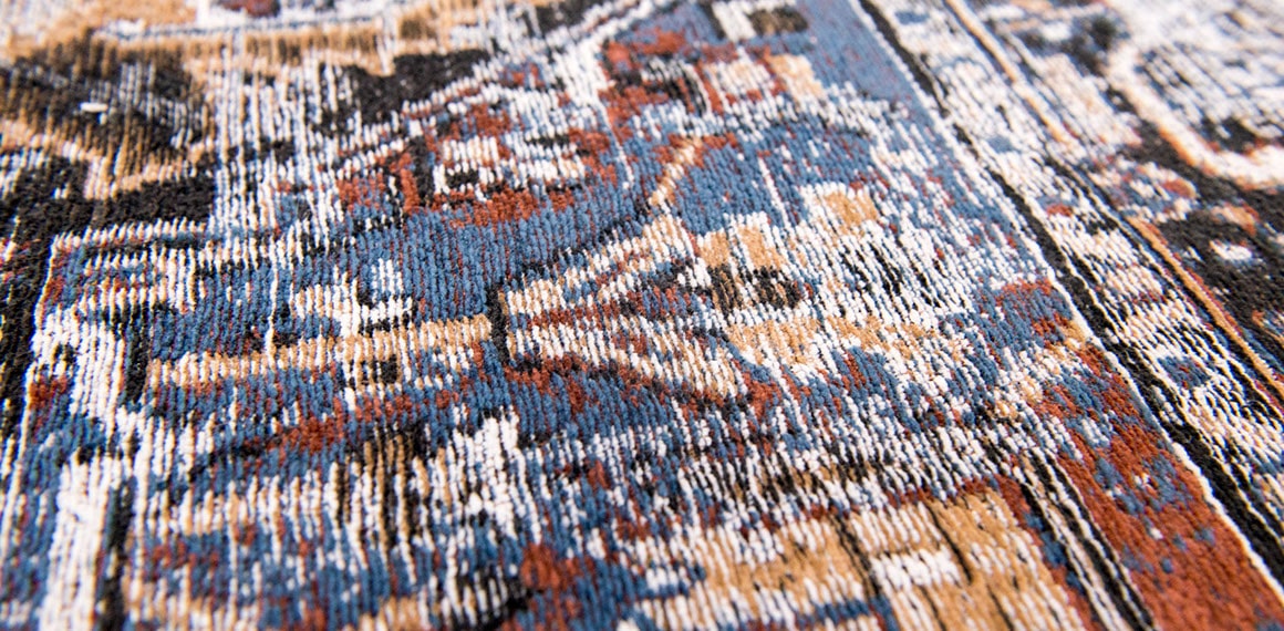 close up of blue detail of faded rug in pale tones and white with brown detail